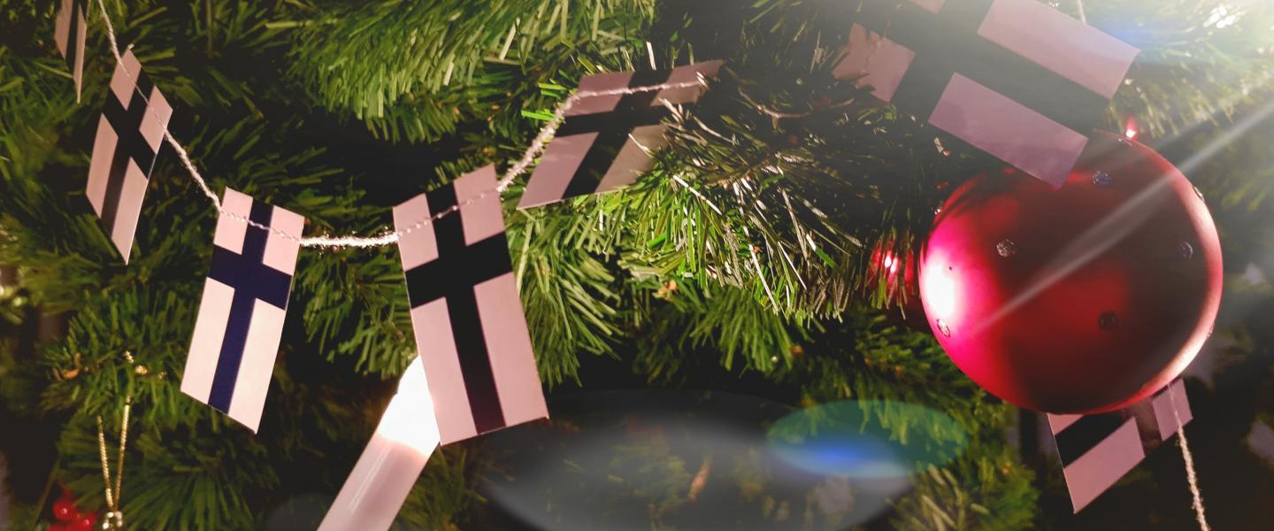 Lähikuva Lehmirannan joulukuusen oksista, joissa Suomen lippujen nauha, punainen kuusenkoriste sekä kynttilöitä.